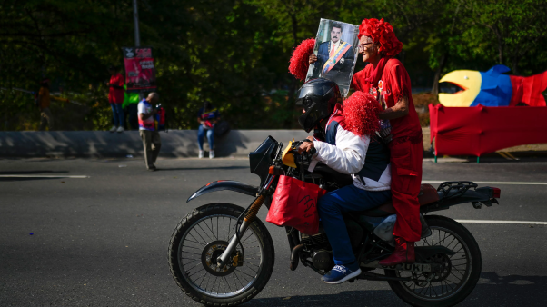 Una partidaria del gobierno viaja en la parte trasera de una motocicleta sosteniendo una imagen del presidente venezolano Nicolás Maduro.