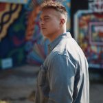 Portrait of Joshua Broome standing against a graffitied wall