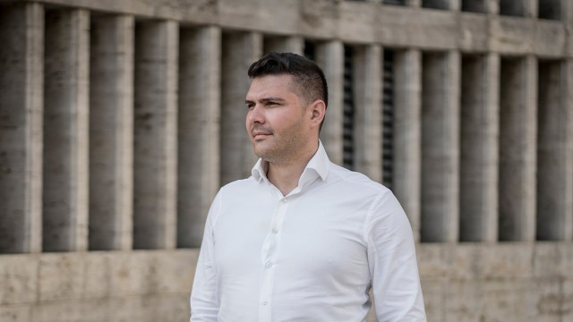 Lucian Mustata stands against a post-Communist architectural concrete building.