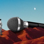 A tiny man next to a huge microphone.